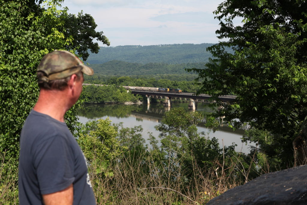 man looking out at a train on a bridge crossing a river