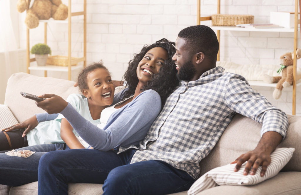 Joyful black family having fun together, relaxing on sofa at home.