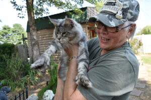 A woman in a hat gently holds a gray and white cat, showcasing a moment of affection and companionship.
